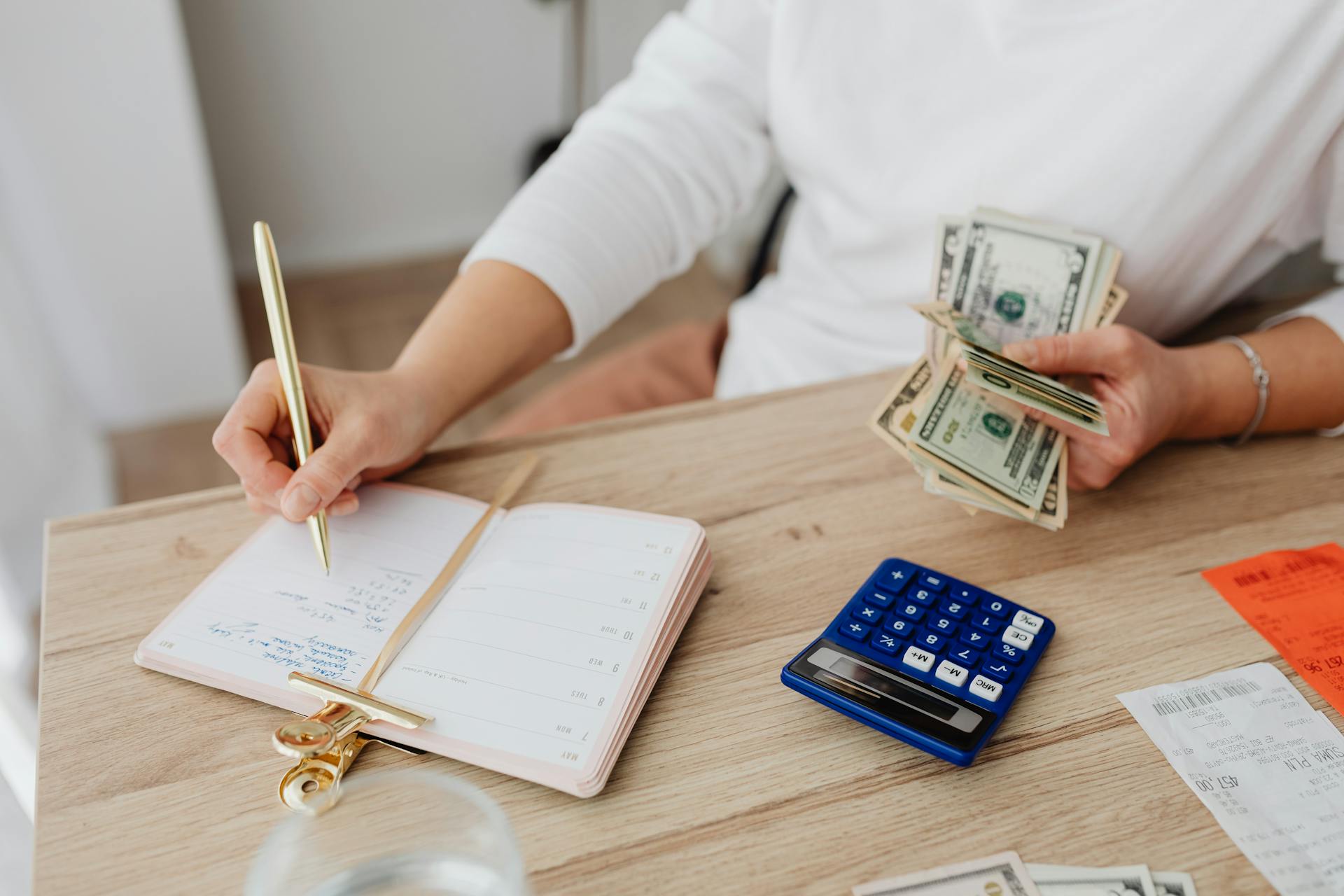 Persoană notând planul lunar de buget cu calculator și bancnote